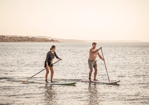 Mature Couple On SUP, Stand Up Paddle Board, Having Fun On Quiet Sea At Sunset