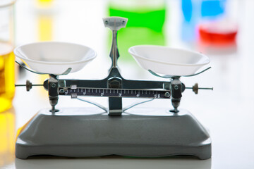 Fototapeta na wymiar Closeup shot of empty black and gray metal weight scales with white trays placed on table in laboratory in blurred colorful reagent in beakers and lab equipment background
