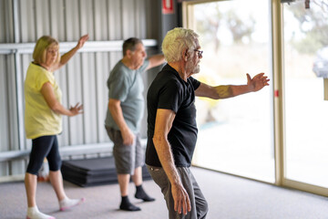 Group of elderly senior people practicing Tai chi class in age care gym facilities.