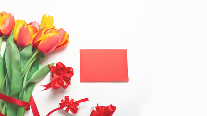Obraz premium A bouquet of fresh tulips with envelope and a gift box with a red ribbon on a white background. Top view. Flat composition. Women lifestyle and holidays concept
