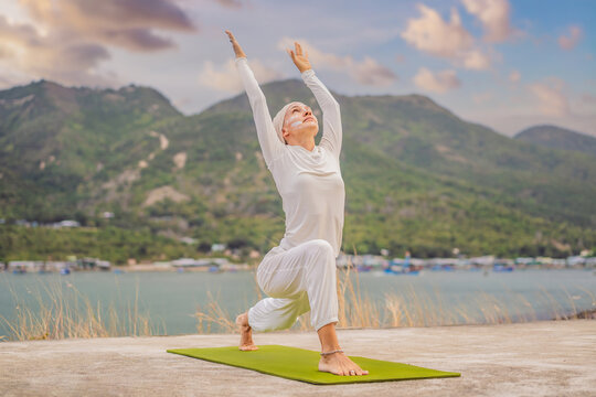 Kundalini yoga woman in white clothes and turban practices yoga kundalini on the background of the sea, mountains and sunset. Fighting face painting of the Indians shows her inner world. Visual