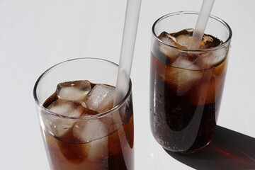 Two glasses of cola with ice cubes on white table background. Top view, copy space. Hard light, shadow. Refreshing summer drink	