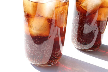 Two glasses of cola with ice cubes on white table background. Top view, copy space. Hard light,...