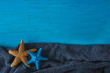 Fototapeta na wymiar Summer beach holidays concept. Frame of two starfishess on dark blue beach towel and blue paint wooden background. Space for text