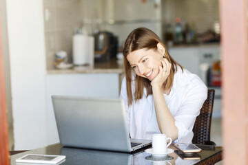 Image of young cheery happy positive, smiling cute beautiful business woman sit indoors in home kitchen office using laptop computer. reading good news