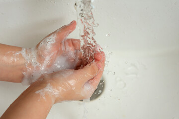 Fototapeta premium The child washes his hands with soap under water in the sink.