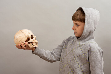 The child holds the skull in his hand and looks at it.