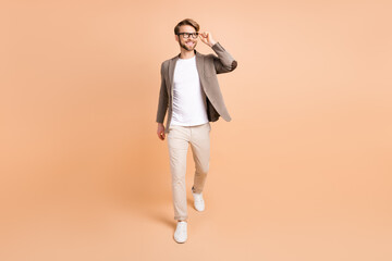 Fototapeta na wymiar Full size photo of attractive dreamy young man walk look empty space smile isolated on beige color background