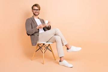 Full size photo of happy handsome attractive charismatic man in glasses relaxing drink tea isolated on beige color background
