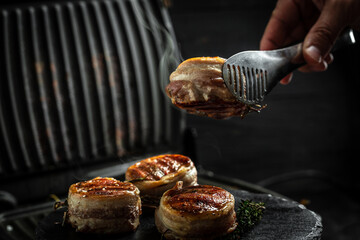 Medallions steaks from the beef tenderloin covered bacon on grill Dark background. Cooking beef...