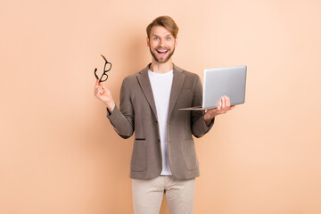 Photo of impressed nice blond hair man hold laptop wear spectacles grey jacket isolated on beige background