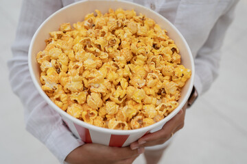 Close-up photo of a young sweet girl, who is holding a tube of popcorn in her hands.