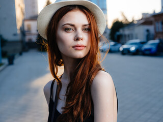 Obraz premium Portrait of a romantic woman in a black dress and in a white hat on the street near buildings