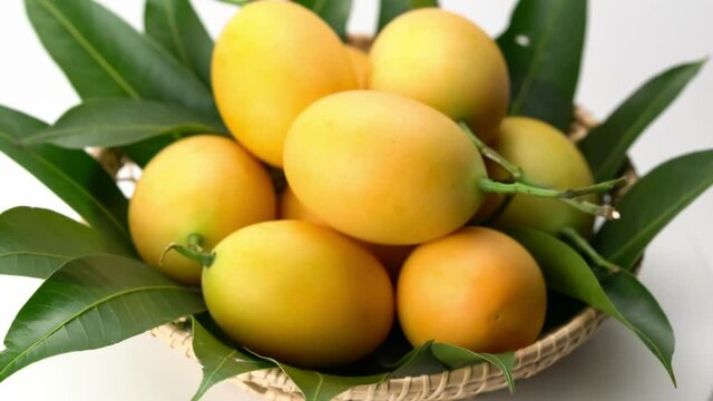 Ripe sweet yellow Marian Plum with leaves in bamboo basket are turning on white background. Popular sweet fruit in Thailand in summer season marian plum with leaves in bamboo basket turning on white.