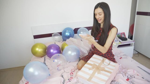 Happy smiling woman holding gift card and sitting on bed with balloons and confetti