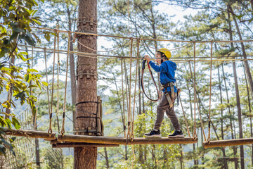 Happy child in a helmet, healthy teenager school boy enjoying activity in a climbing adventure park on a summer day