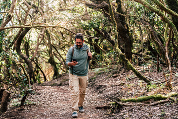 Adult man walk in the woods and use modern internet 5g technology with phone - hipster mature male people explre and enjoy adventure alone with backpack and woods around