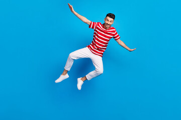 Fototapeta na wymiar Photo of sweet attractive young man wear striped t-shirt jumping high arms sides isolated blue color background