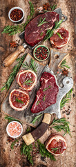 Fototapeta na wymiar Variety of raw beef meat steaks for grilling with seasoning on over meat butcher knife. banner, menu recipe top view vertical image