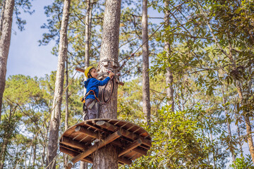 Happy child in a helmet, healthy teenager school boy enjoying activity in a climbing adventure park on a summer day