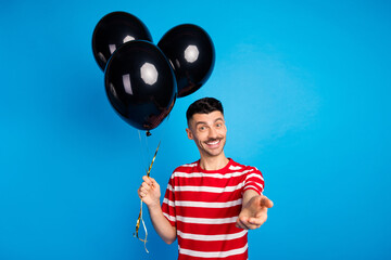 Photo of happy attractive positive young man invite you good mood hold balloons decoration isolated on blue color background