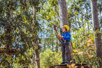 Happy child in a helmet, healthy teenager school boy enjoying activity in a climbing adventure park on a summer day