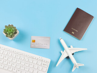 flat lay of airplane model, computer keyboard, passport, credit card and cactus on blue background, business and traveling concept.