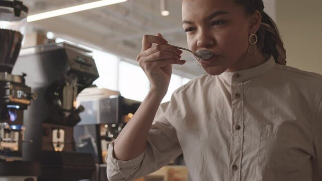 Tilt up of professional female bartender standing at worktop in cafe and tasting different types of coffee in cup tasters in restaurant. Coffee degustation