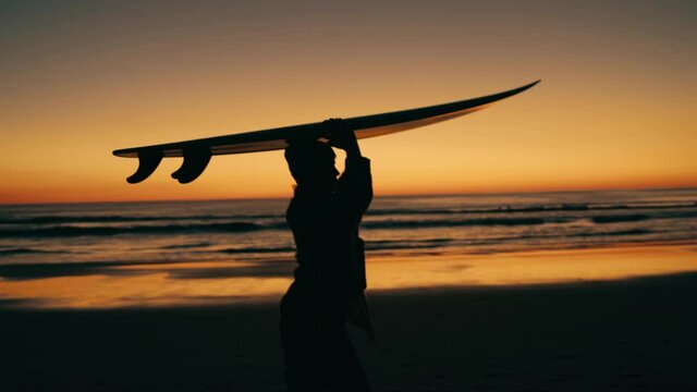 Handheld shot of professional female surfer carry surfboard back to van after long day of surfing. Last rays of sun on epic travel destination beach. Concept vanlife and surfing lifestyle