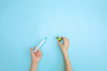 A child's hand holds a syringe on a blue background with a copy space