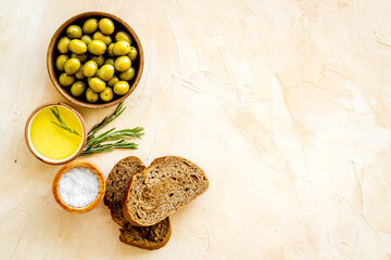 Olives in wooden bowls with sliced bread and oil, top view