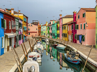 Fototapeta na wymiar Boats and colorful houses in a canal street houses on Burano island, Venice, One unrecognizable people on the background.