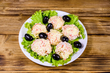White plate with crab-cheese balls and lettuce leaves on wooden table