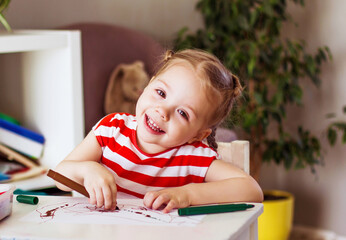 Little smiling children girl sits at the table and draws with felt-tip pens, happy childhood