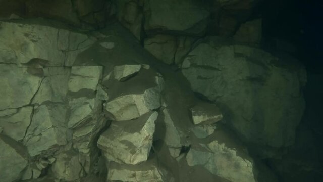 The camera slowly lowers along a rocky cliff at the base of which an underwater pipeline is laid.