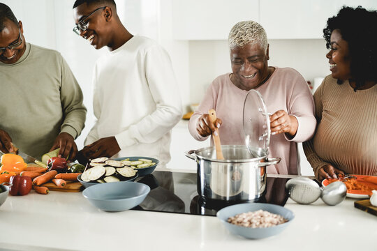 Happy black family cooking vegan food inside kitchen at home - Focus on mother face