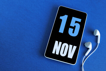 November 15. 15 st day of the month, calendar date. Smartphone and white headphones on a blue background. Place for your text. Autumn month, day of the year concept
