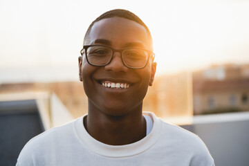 Happy young african man looking at camera outdoors at summer sunset - Focus on face