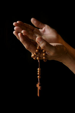 Praying hands of Indian Catholic woman with wooden rosary isolated on a black background.