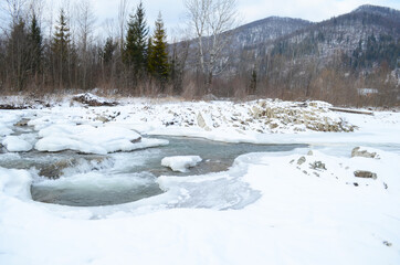 A frozen river in a wintry landscape. Winter landscape with forest, cloudy sky and sun.