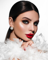 Portrait of a woman. The beauty. Professional makeup. Long eyelashes. Red lipstick. Shawl made of white feathers. Brunette.