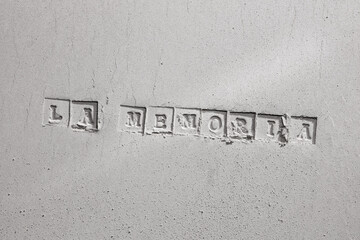 Print of the Spanish word "MEMORY" is written on a cement background. 