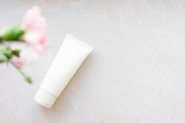 Fototapeta na wymiar white cosmetic tube with face cream, body lotion or cleanser on a light background with pink flowers. Sensitive skin care concept. Copy space