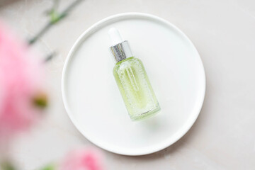 face serum on a plate with pink flowers on a light background. Sensitive skin care concept.
