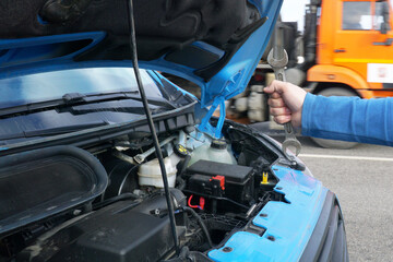 Fototapeta premium A man's hand with a wrench over a car engine with an open hood. The concept of breakdown and repair in transit.