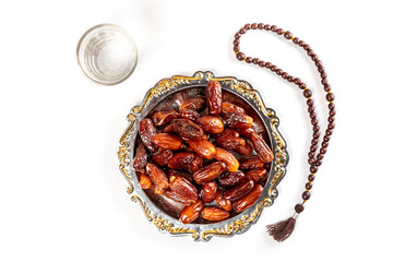 Vintage bowl of dates with a glass of water. Dates in a bowl and islamic prayer beads. Date palm fruits or kurma, ramadan on white background. Ramadan kareem with dates