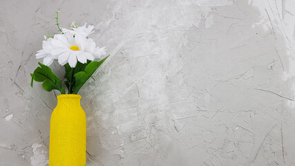 bouquet of artificial daisies in a yellow vase on a concrete background
