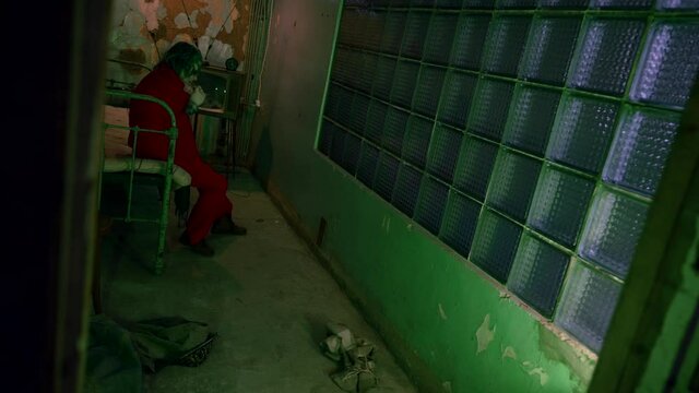 A depressive clown in a red suit smokes and is nervous in a nightmare room with a bed. Throwing things around is freaking me out