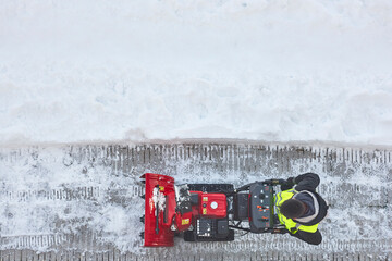 Worker cleaning snow on the sidewalk with a snowblower. Wintertime