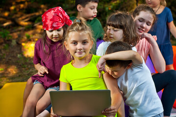 Children play in nature with a laptop. Boys and girls are resting in a tent camp. Children sit on a purple inflatable sofa in summer.